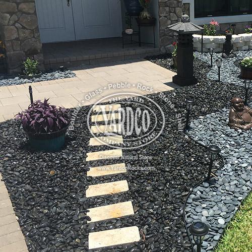 Landscape bed with Coral Stone Stepping Stones, Peruvian Black Beach Pebbles, and 3/4" High-Polished Beach Pebbles